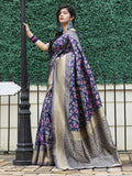 Woman in navy floral saree with gold border, standing by lamp post against green hedge