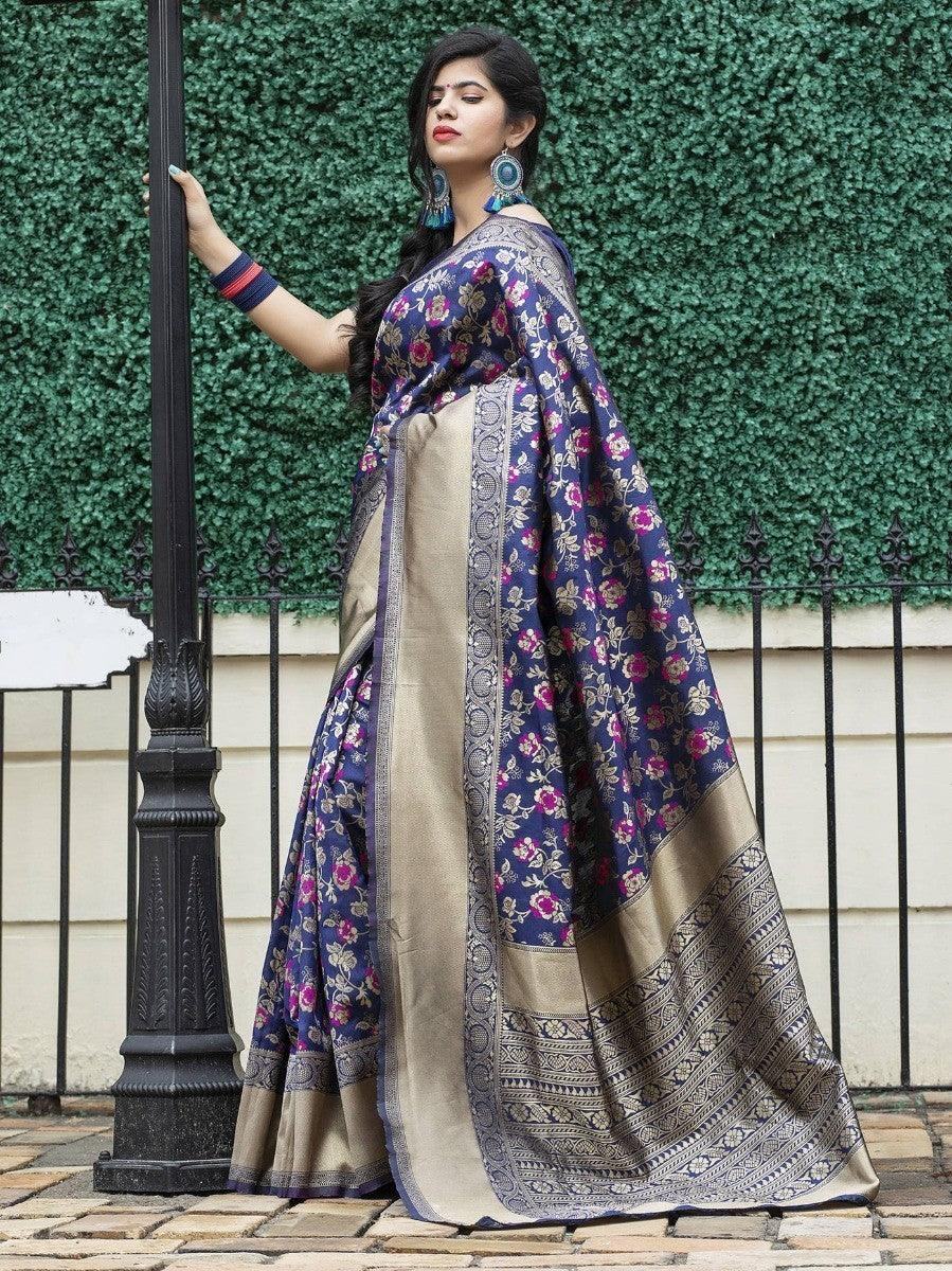 Woman in navy floral saree with gold border, standing by lamp post against green hedge