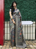 Woman wearing floral printed saree with gold border, standing by green hedge and red door