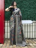 Woman in elegant floral saree with gold border, standing by red door and green hedge, fashion outfit