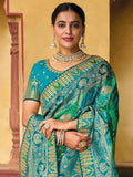 Woman in teal and green embroidered saree with gold jewelry, traditional Indian fashion