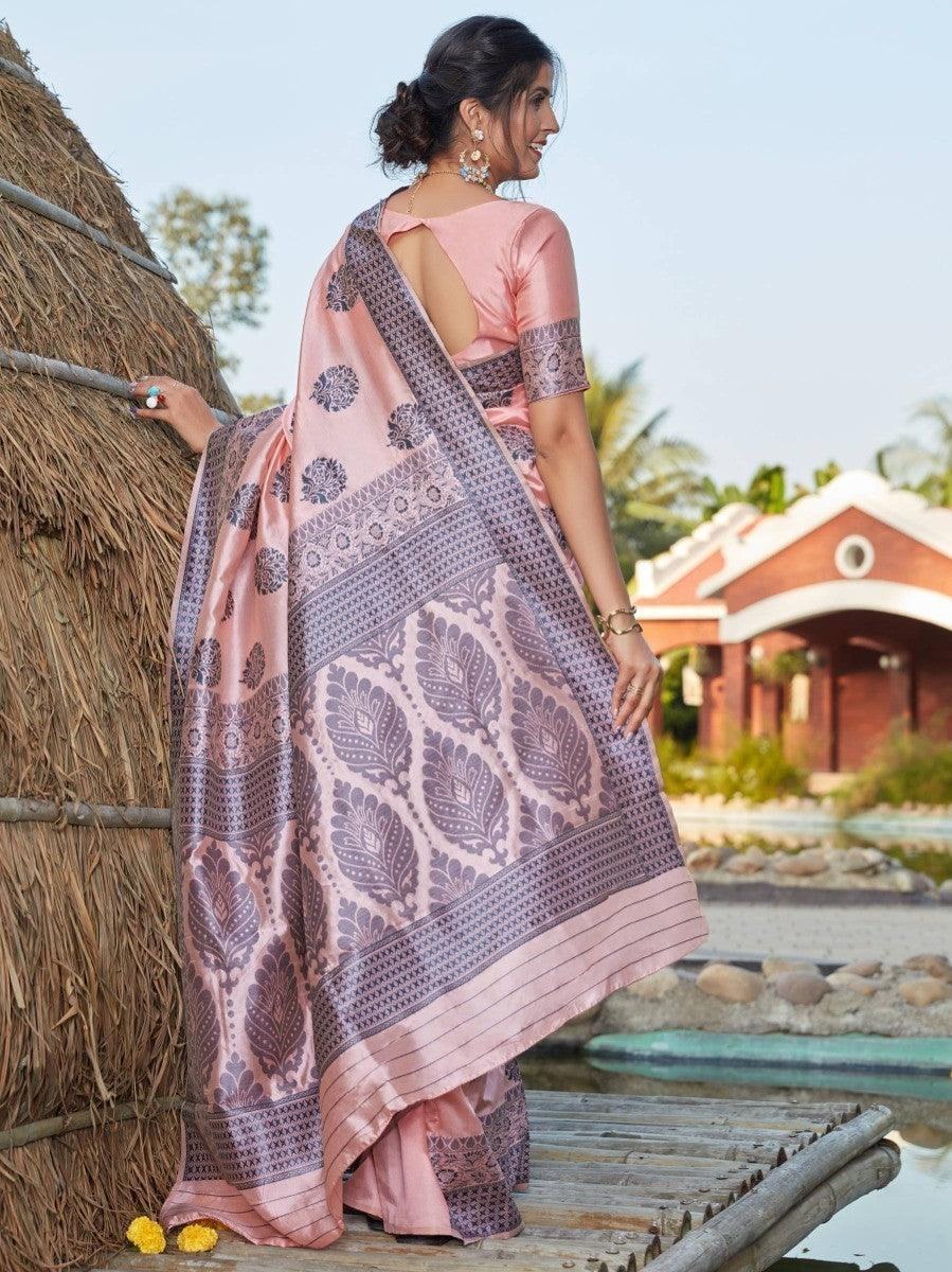 Woman in pink saree with purple leaf print, standing on wooden bridge near thatched hut