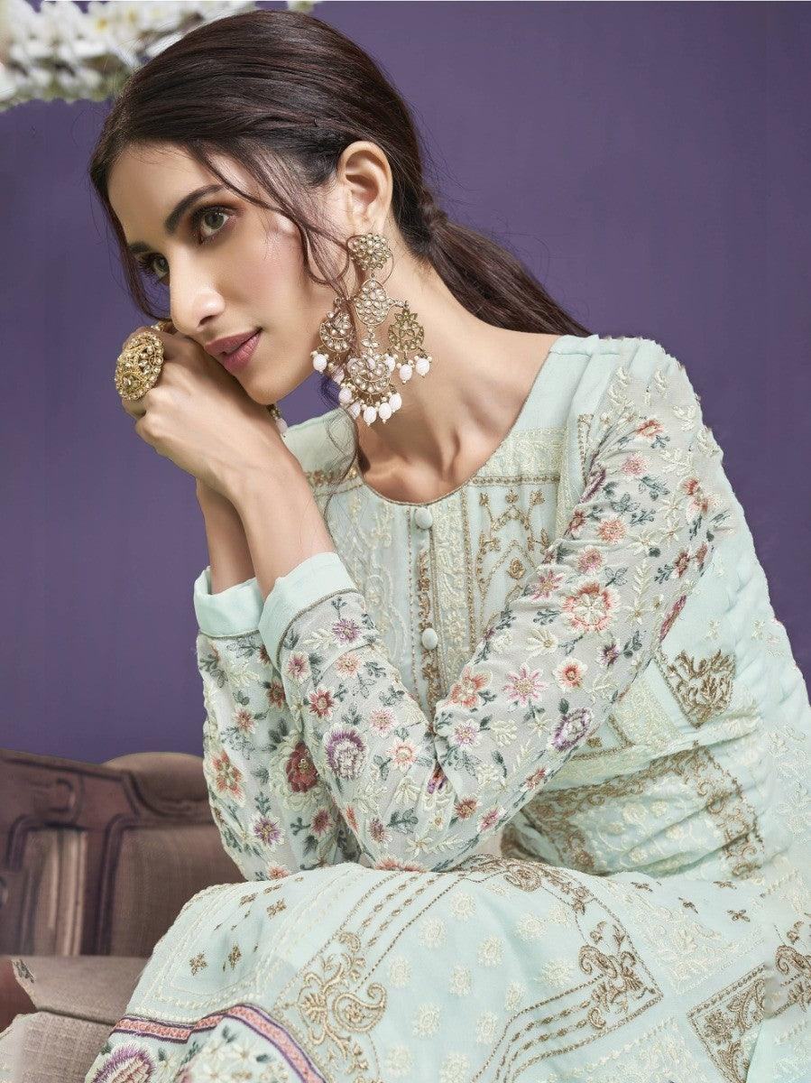 Woman in mint green floral embroidered dress with gold detailing and statement earrings