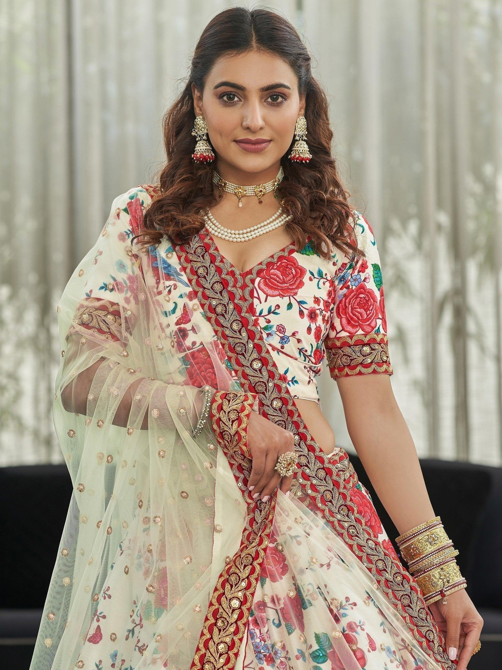 Woman in floral embroidered lehenga with red gold detailing, pearl jewelry, and sheer dupatta for festive occasions